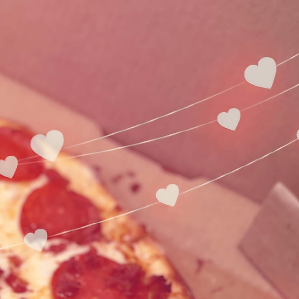 Close-up of a pepperoni pizza in a box with heart-shaped decorations on strings.