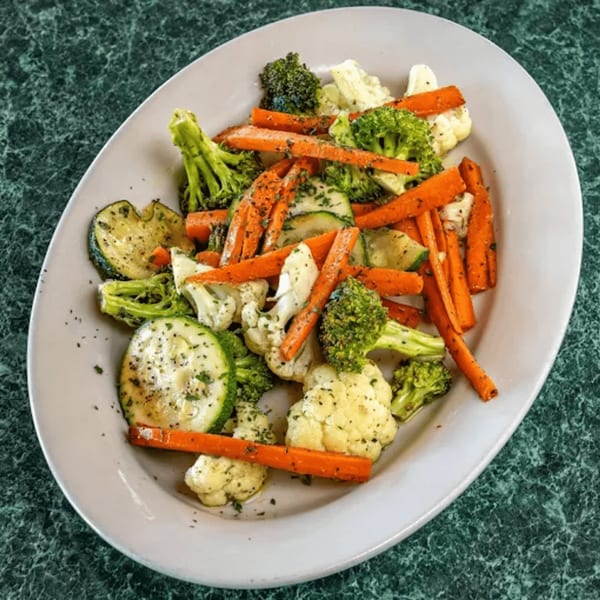 A white oval plate filled with steamed vegetables including carrots, broccoli, cauliflower, and zucchini.