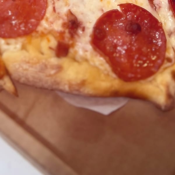 Close-up of a slice of North Beach Pizza pepperoni pizza with melted cheese in a box.