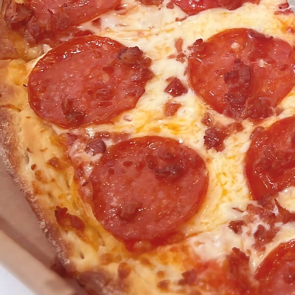 Close-up of a North Beach Pizza pepperoni slice with melted cheese and crispy crust.