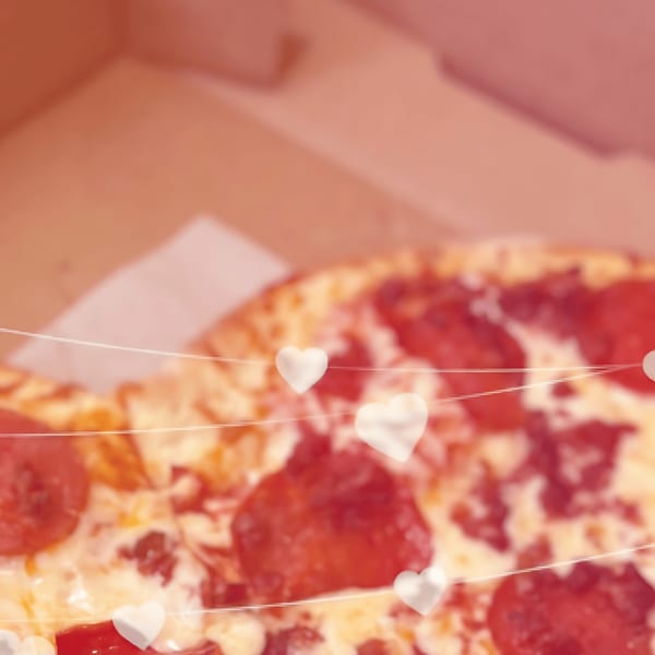 Pepperoni pizza in a box with white heart decorations and string lights, with a pink overlay.