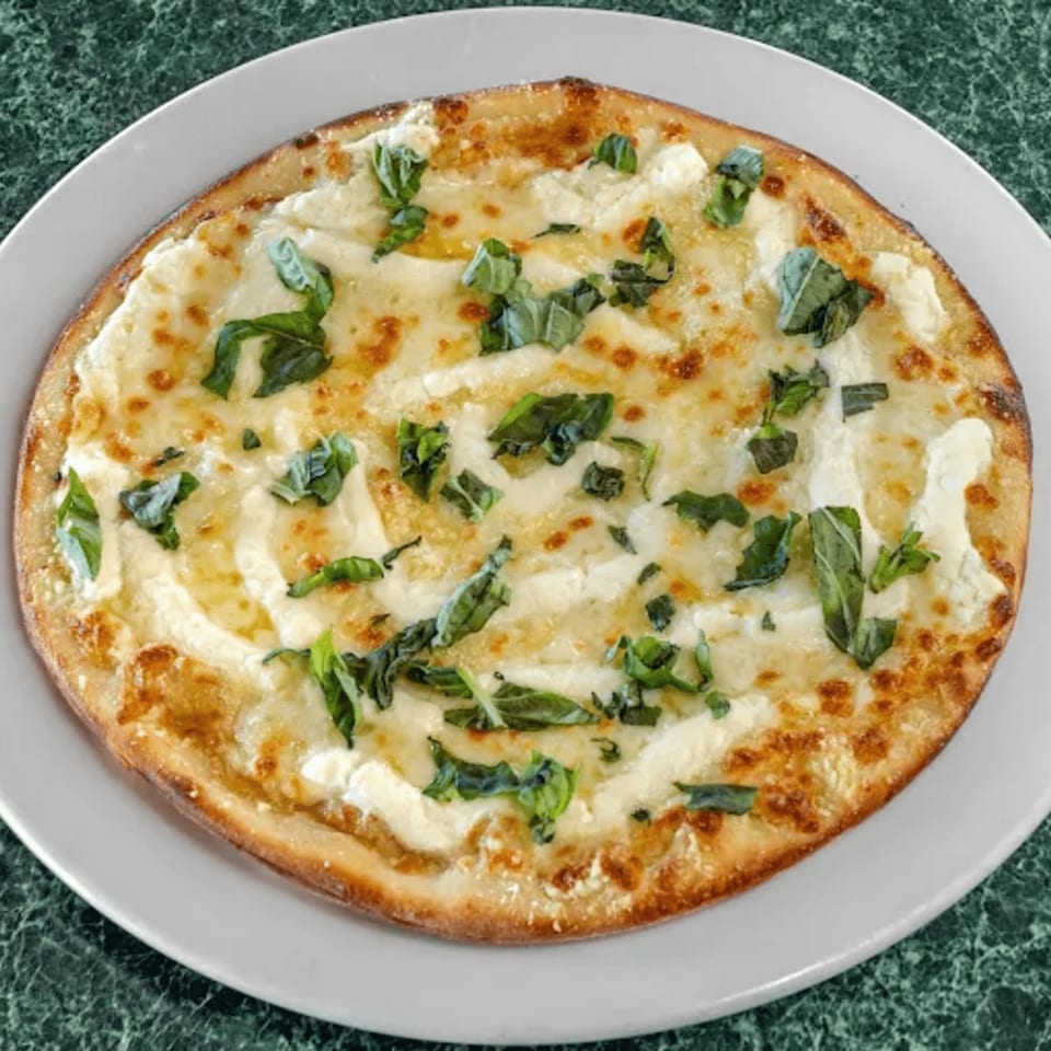 North Beach Pizza's white pizza with melted cheese and fresh basil on a white plate.