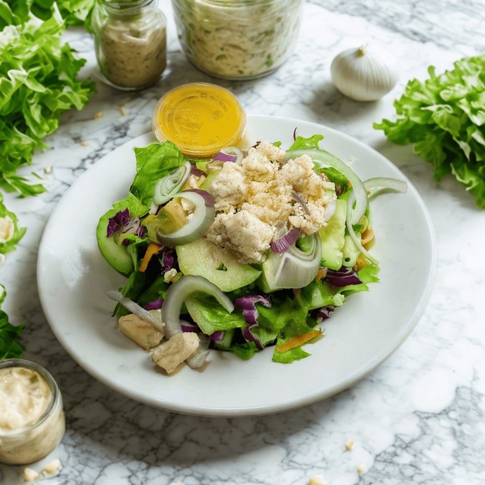 Fresh green salad with red onion, cucumber, and crumbled feta cheese, with dressing on the side.