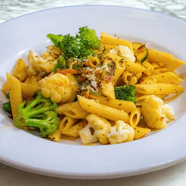 Penne pasta with broccoli, cauliflower, and zucchini, topped with herbs and grated cheese.