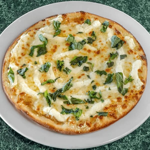 North Beach Pizza's white pizza with melted cheese and fresh basil on a white plate.