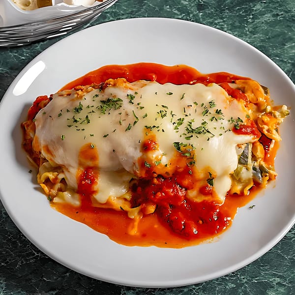 Baked lasagna with melted cheese, red sauce, and parsley on a white plate.
