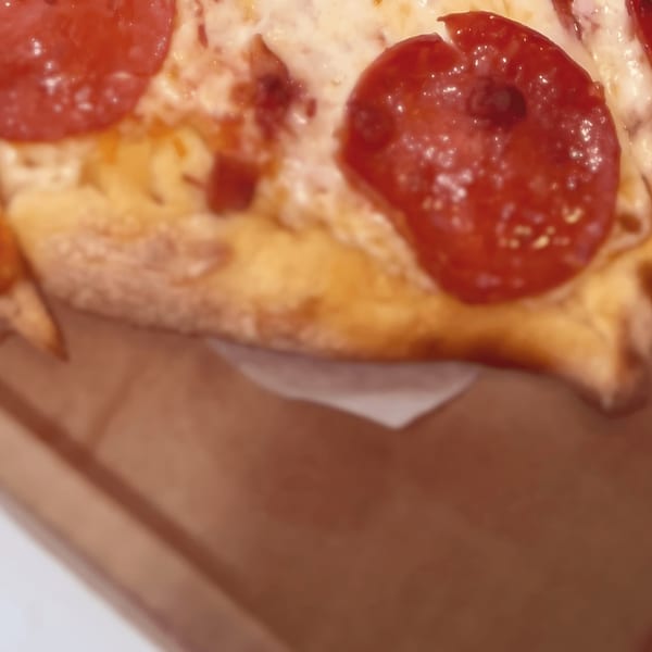 Close-up of a pepperoni pizza slice with melted cheese in a brown pizza box.