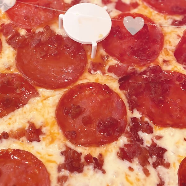 Close-up of a pepperoni pizza with a white plastic pizza saver and a small heart.