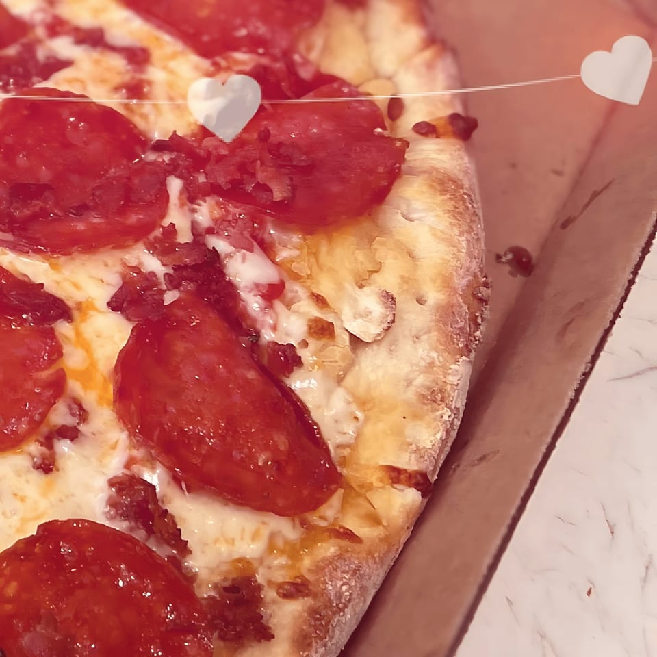 Close-up of a pepperoni pizza with melted cheese and a thick crust, with heart decorations.