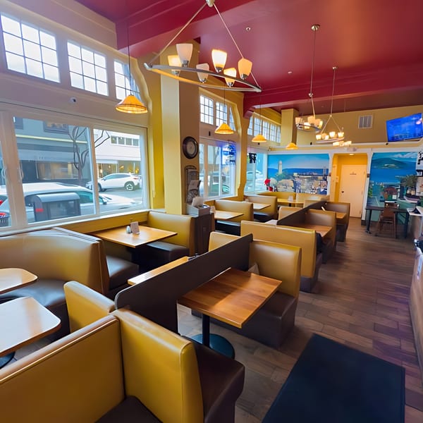 Interior of North Beach Pizza with yellow booths, wooden tables, and a mural of a coastal town.