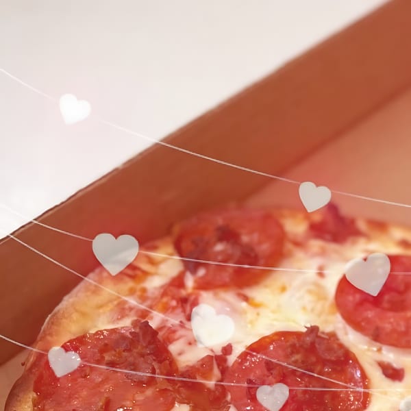Close-up of a pepperoni pizza in a North Beach Pizza box, with heart-shaped lights.