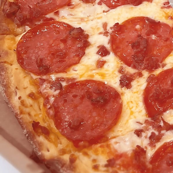 Close-up of a North Beach Pizza pepperoni slice with melted cheese and crispy crust.