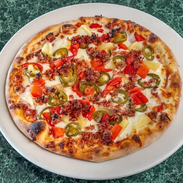 A North Beach Pizza with red peppers, pineapple, jalapeños, and crumbled sausage on a white plate.